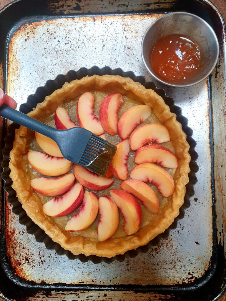 Brushing apricot jam onto nectarines in tart