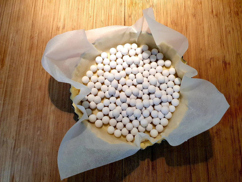 Lined tart pastry with pie weights ready to blind bake