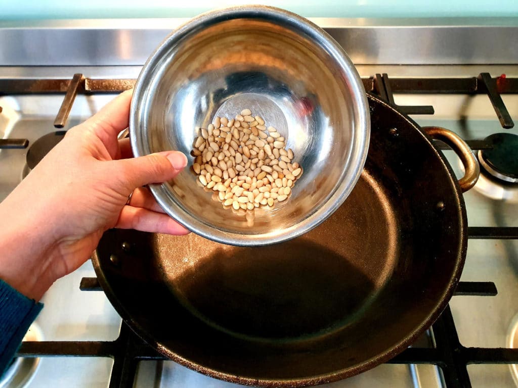 Tipping pine nuts into dry frying pan