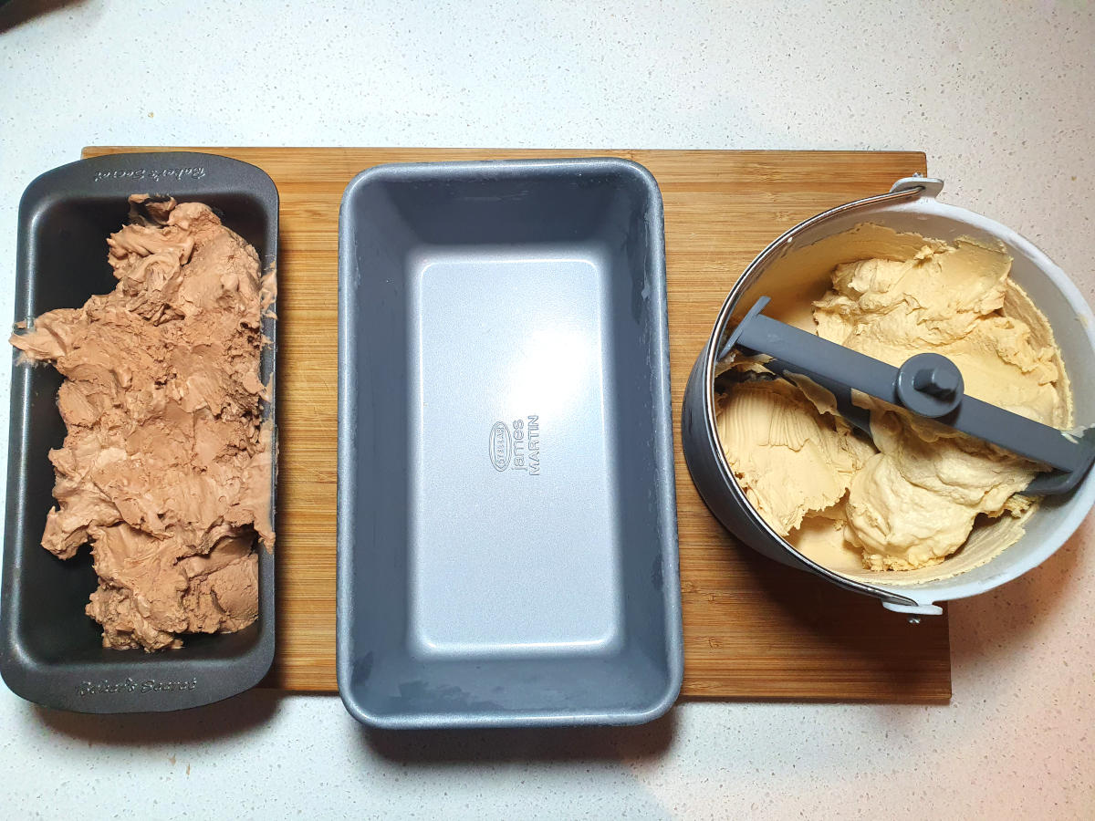 top down view of Nutella ice cream in loaf pan, empty loaf pan and peanut butter ice cream in churning bucket, on a chopping boar, on a bench.