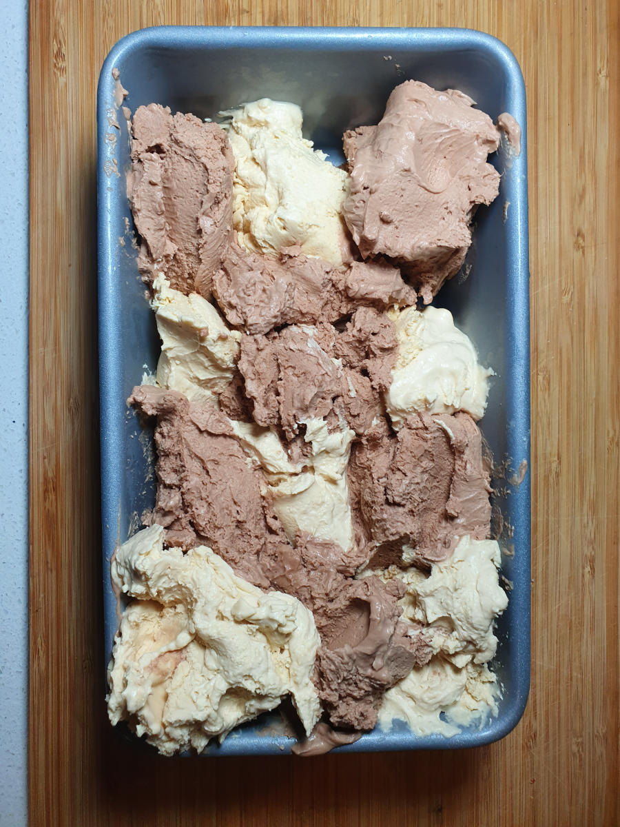 Top down view of Nutella peanut butter ice cream assembly pattern in loaf pan, on a chopping board.