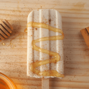 Single cinnamon, honey and kefir popsicle with honey drizzle and sprinkle of cinnamon, cinnamon stick, honey stick and honey bowl, on chopping board