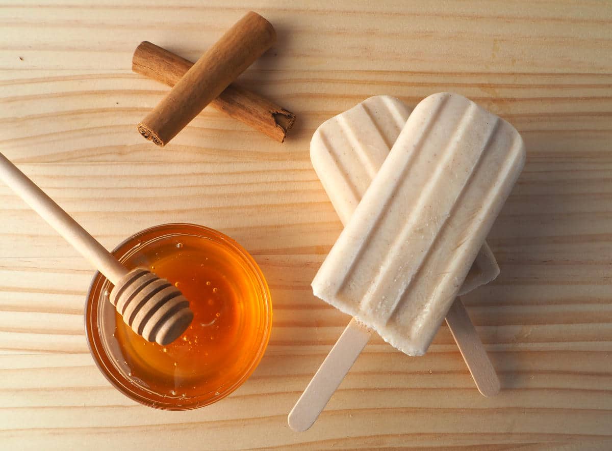 Stack of two cinnamon, honey and kefir popsicles with stacked cinnamon sticks, honey in dish and honey stick, on chopping board