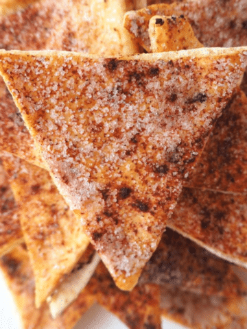 close up of pile of cinnamon sugar pita chips on a while plate.