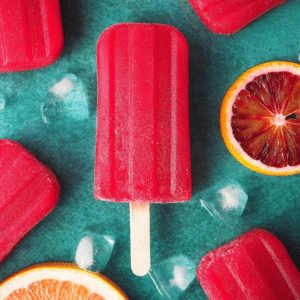 Ruby grapefruit and blood orange popsicle close up with orange and grapefruit slices and ice cubes on green background