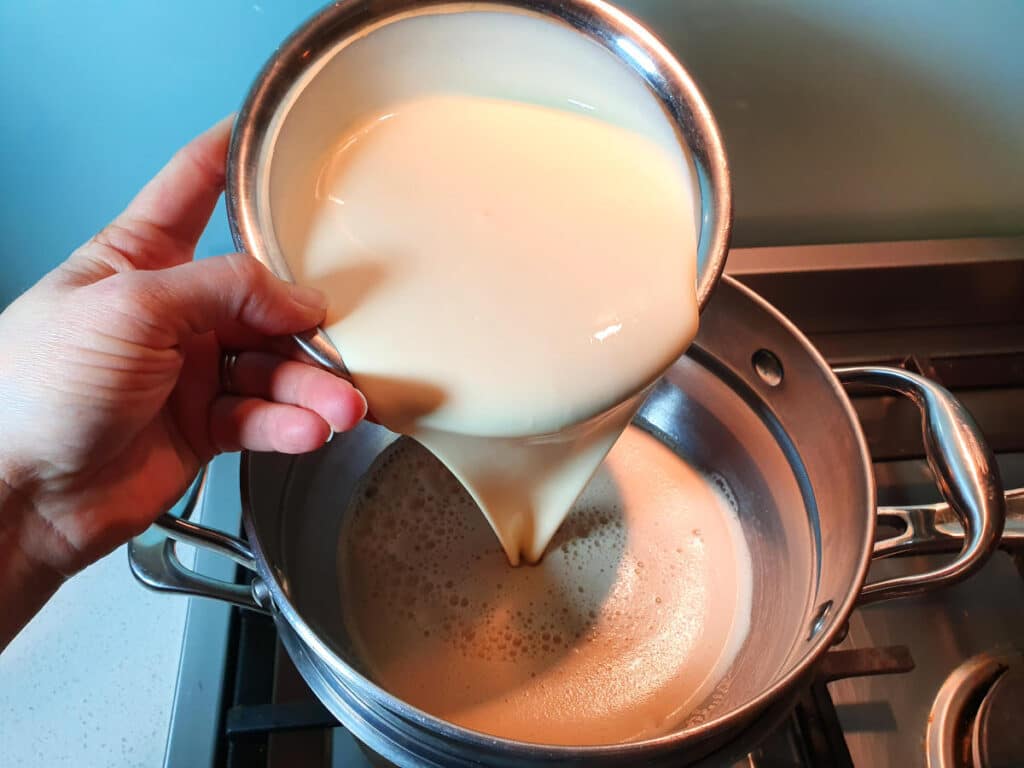 Adding cream to milk and tea mix in double boiler on stove top