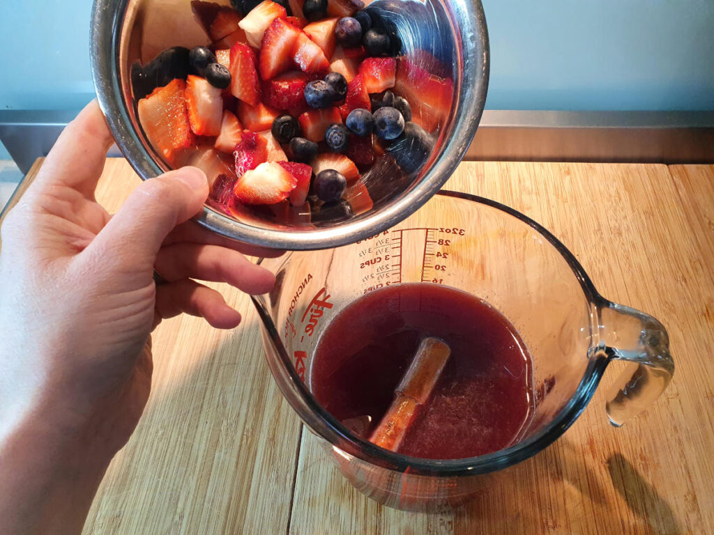 adding chipped fruit to jug of sangria popsicle mix