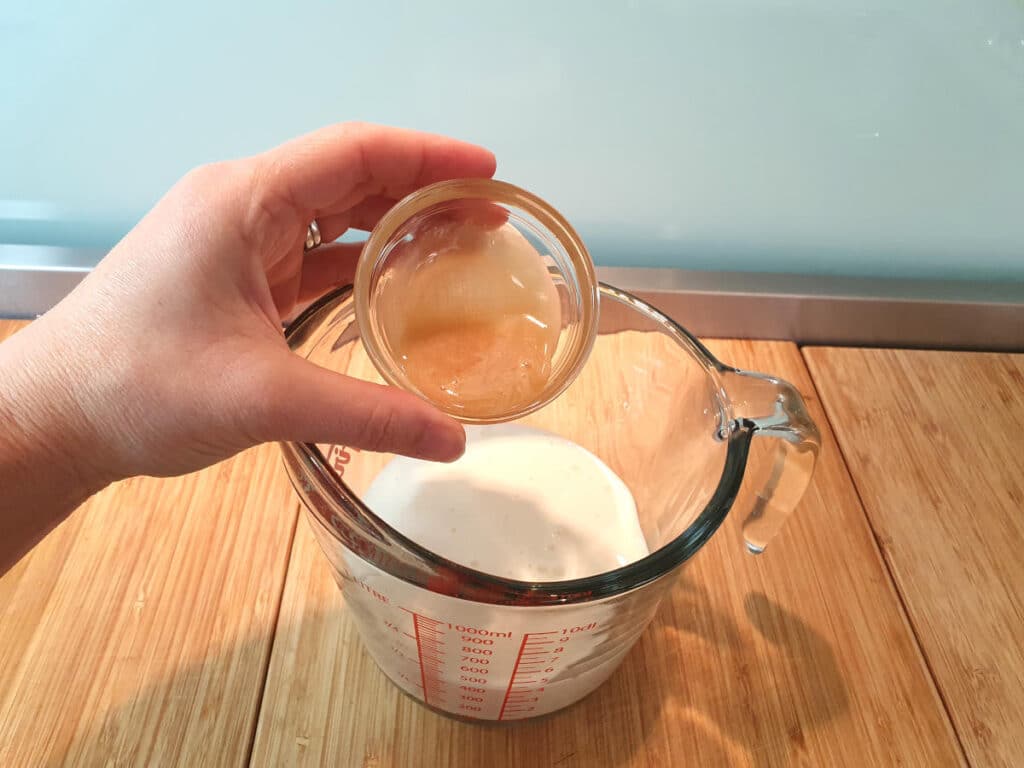 Adding honey to jug with kefir in it, on a brown board