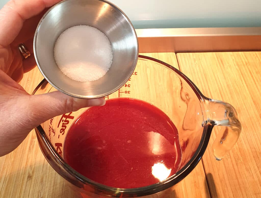 Adding sugar to jug of grapefruit and orange juice mix for popsicles