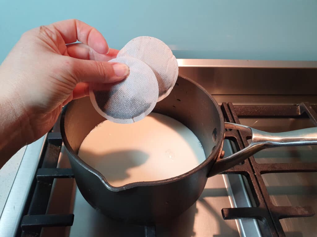 Adding tea bags to warm milk in pan on stove top