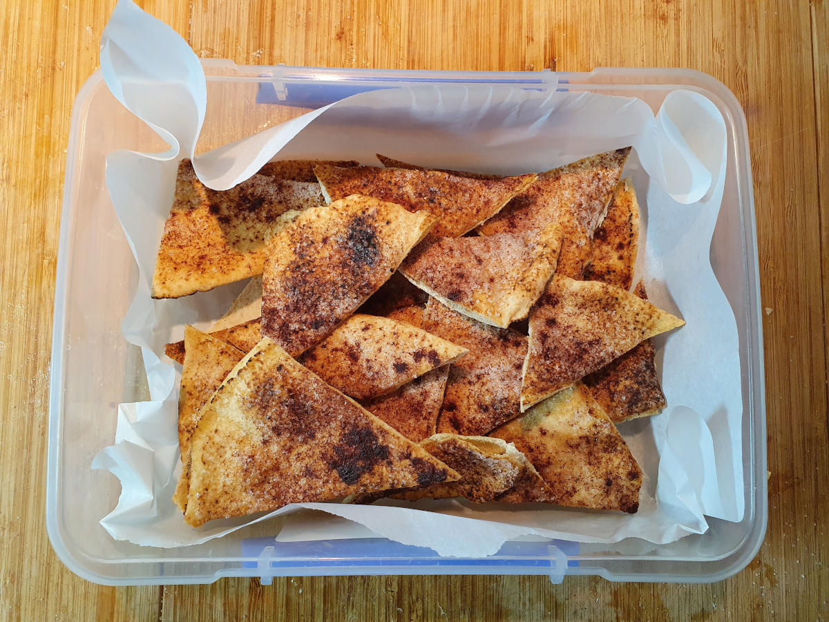 cinnamon sugar chips in large air tight container lined with baking paper with the lid off showing the contense, top down view.