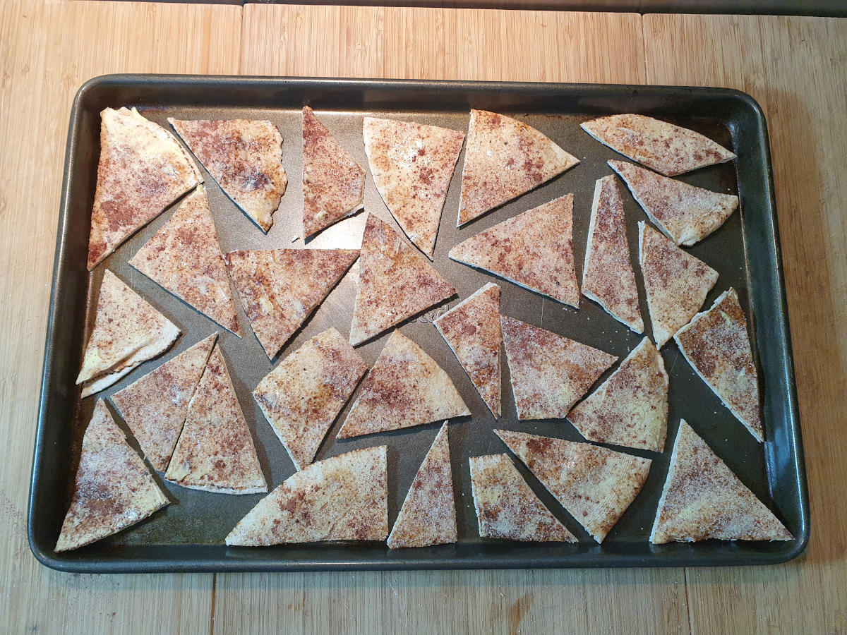 pita chips laid out on a tray ready for baking, on a chopping board.