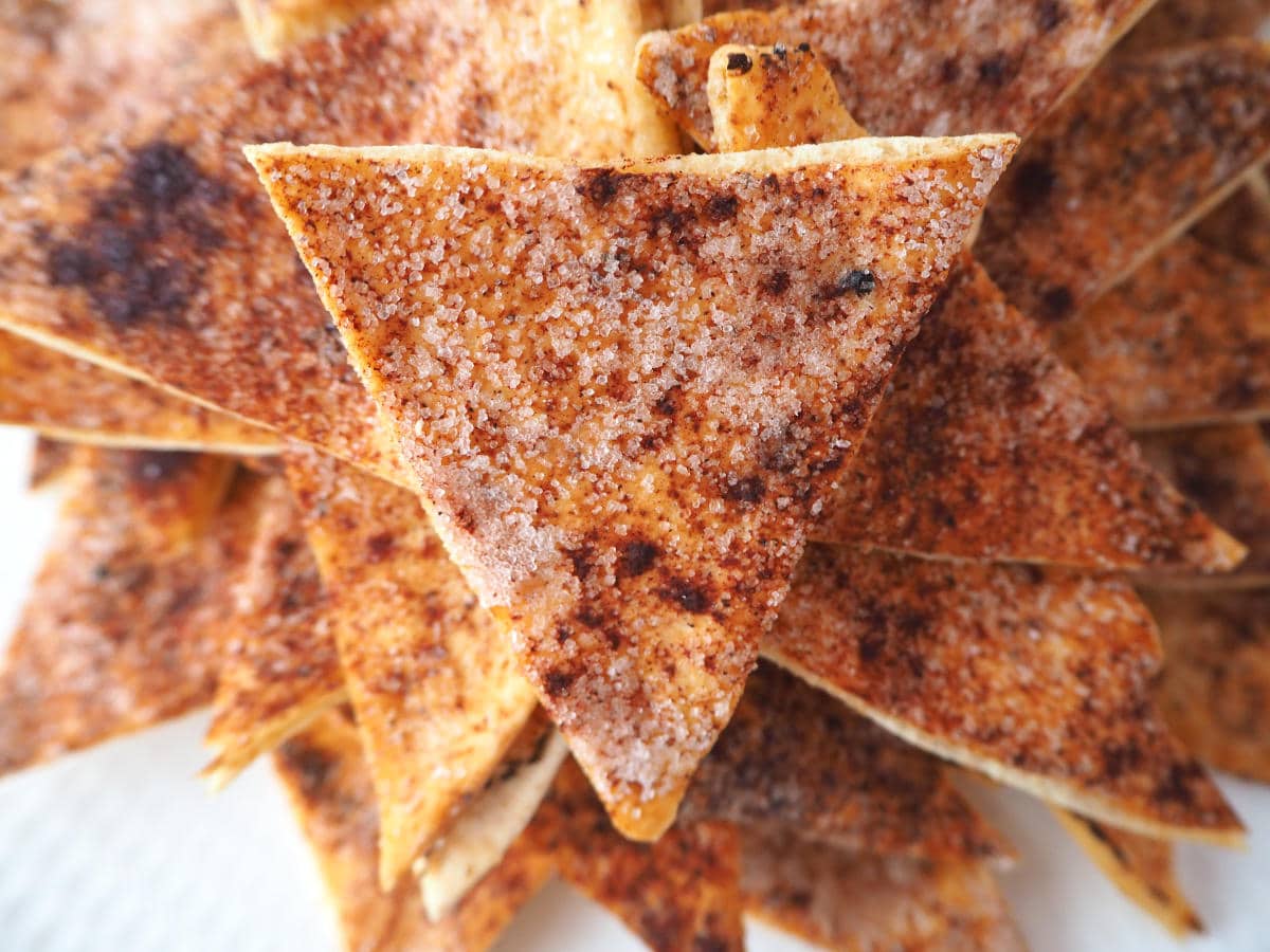 close up of pile of cinnamon sugar pita chips on a while plate.