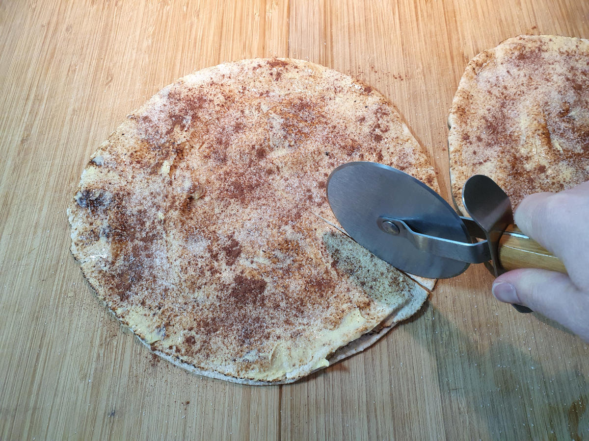 cutting up pitta bread on a chopping board with a pizza cutter.