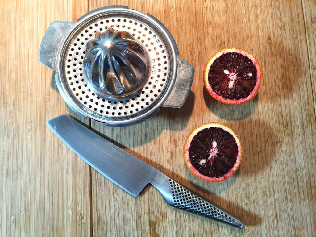 blood oranges on board with knife and juicer ready to juice