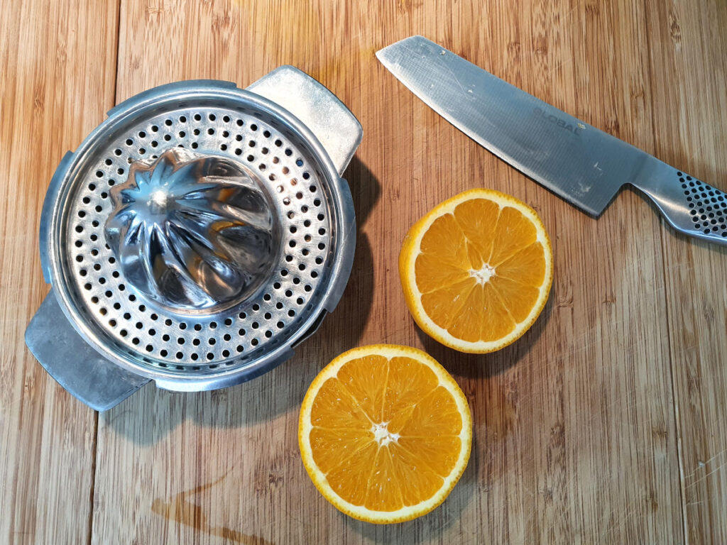 one orange cut in half on a chopping board with a knife and a juicer ready to be juiced