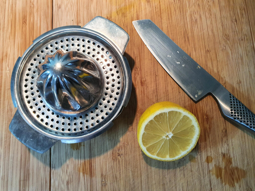 one lemon orange cut in half on a chopping board with a knife and a juicer ready to be juiced