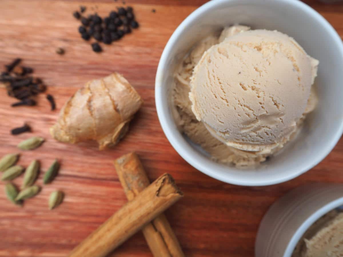 Scoop of chai ice cream vin a white bowl, on a brown board with spices next to it, viewed top down