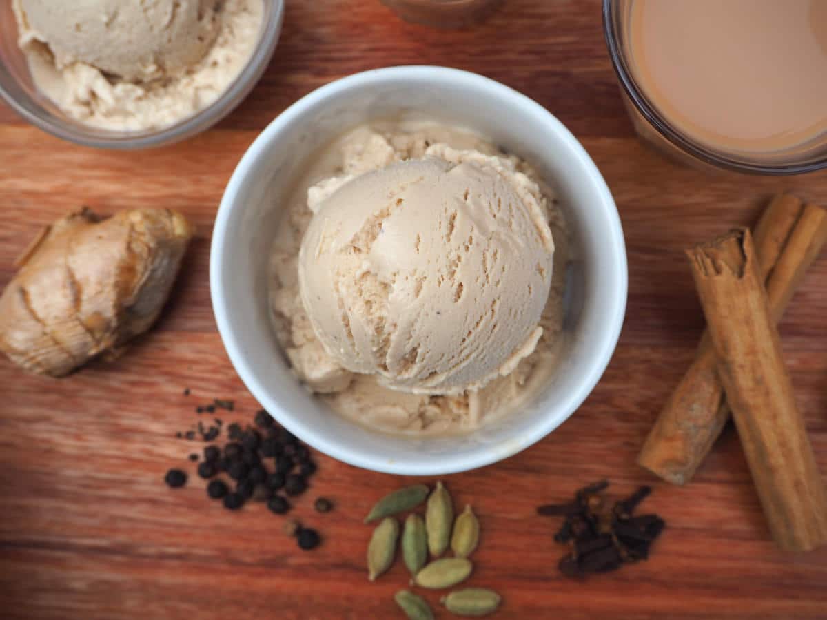 Scoop of chai ice cream vin a white bowl, on a brown board with spices and cup of tea next to it, viewed top down