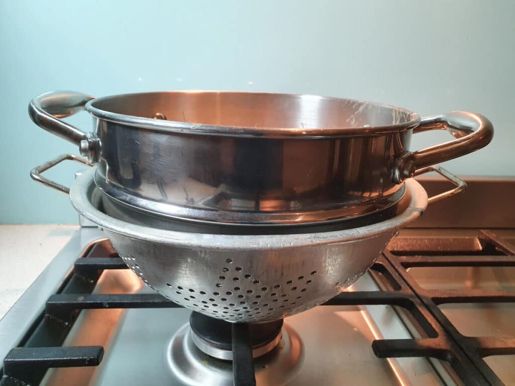 resting double boiler top in colendar on stove top