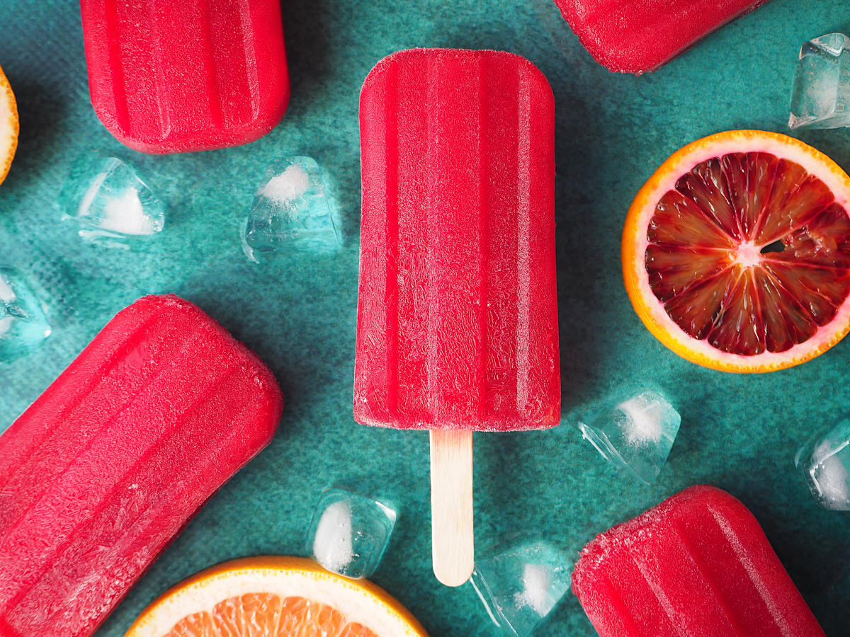 Ruby grapefruit and blood orange popsicle close up with orange and grapefruit slices and ice cubes on green background