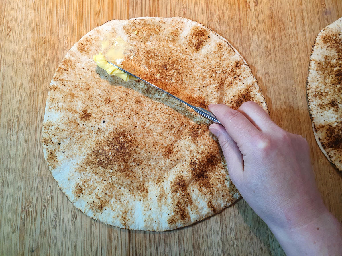 spreading butter on a pita bread on a chopping board.