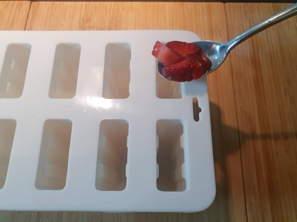 transfering chopped fruit to popsicle moulds with a spoon
