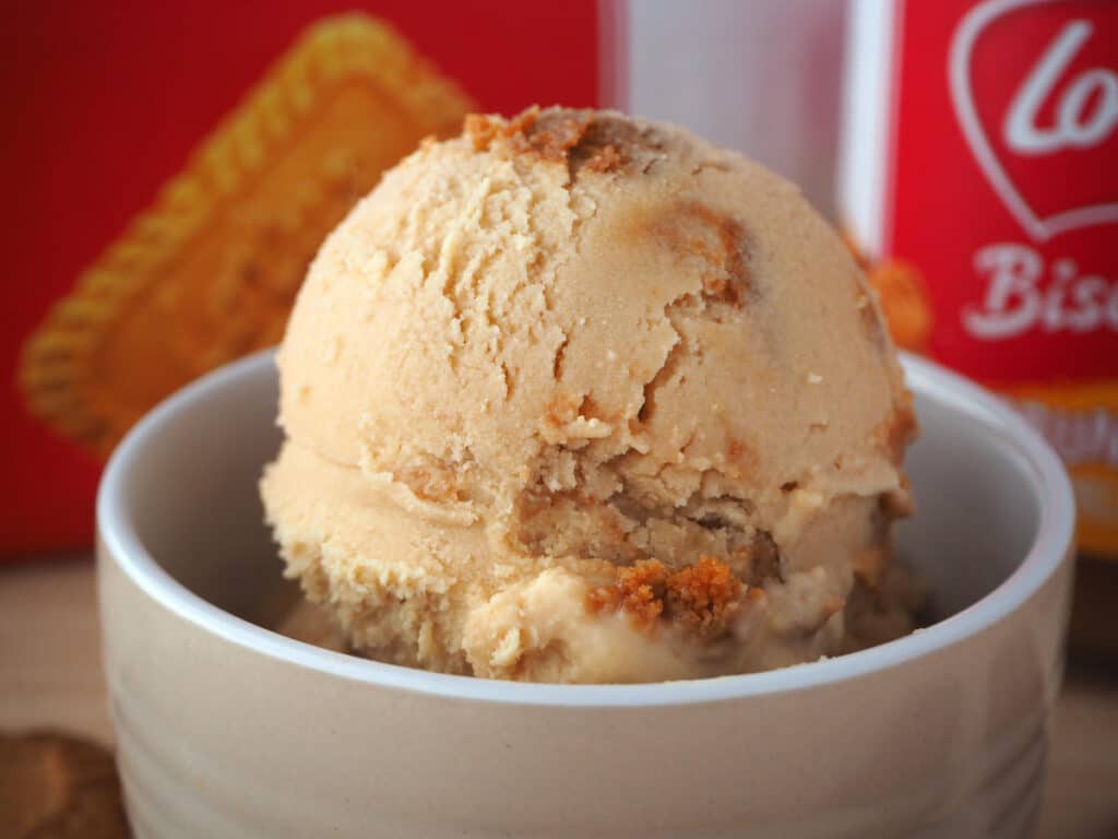 Side view close up of scoop of biscoff ice cream with biscoff jar and packet of biscoff biscuits in the background.