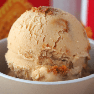 Side view close up of scoop of biscoff ice cream with biscoff jar and packet of biscoff biscuits in the background.