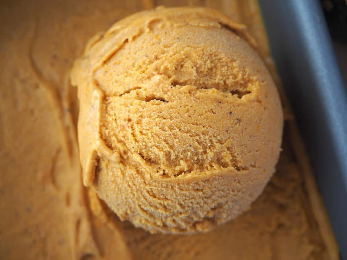 Very close up view of scoop of pumpkin spice ice cream in a pan, showing ice cream texture or bark.
