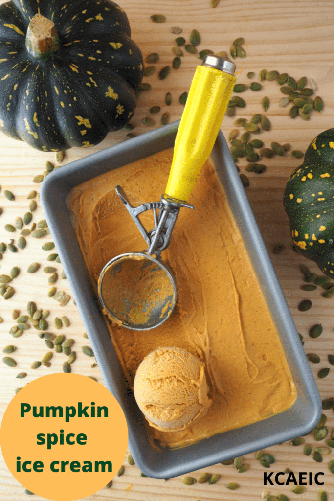 top down view of pumpkin spice ice cream in a loaf pan, with a scooped ice cream and ice cream scoop, on a wooded background with two pumpkins on the side and pumpkin seeds scattered around, and text overlay, pumpkin spice ice cream and KCAEIC.