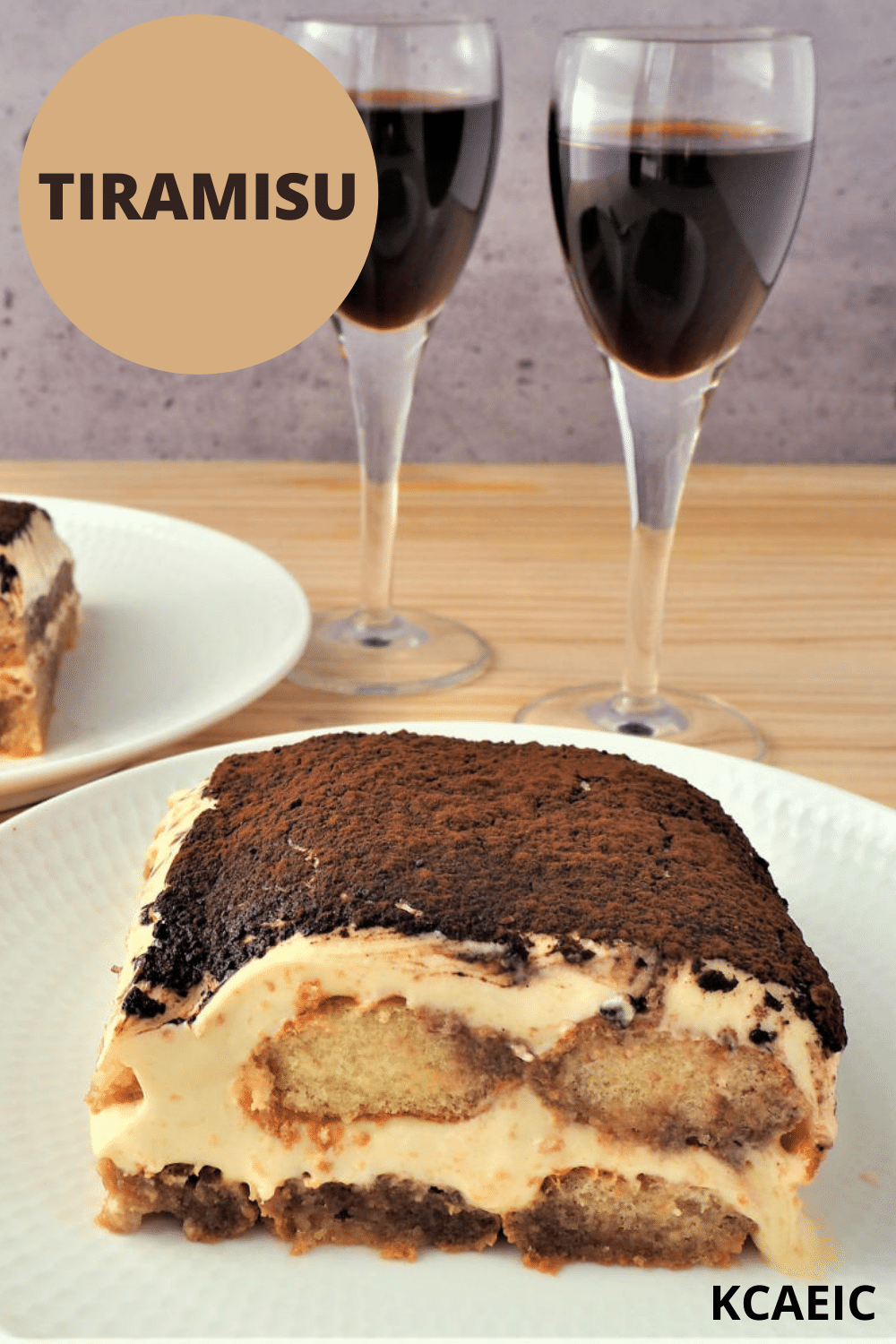 Tiramisu 23 tiramisu on white plate with two small glasses of marsala wine, with a second serve in the background, with text overlay, tiramisu and KCAEIC.