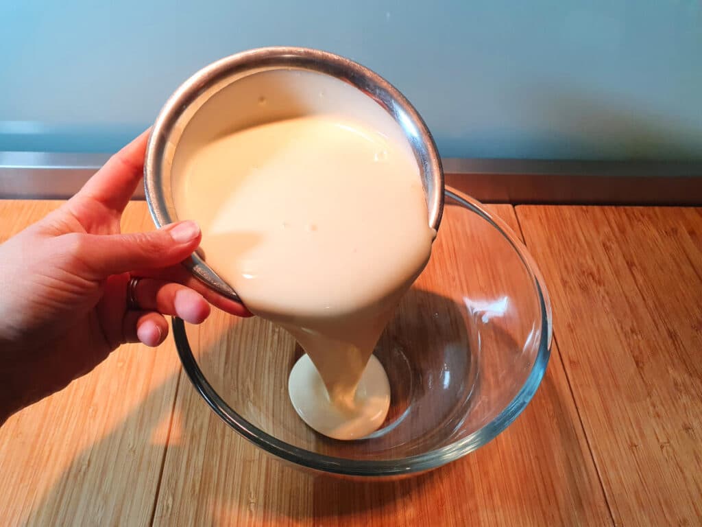 adding cream to a glass bowl, on a wooded chopping board.