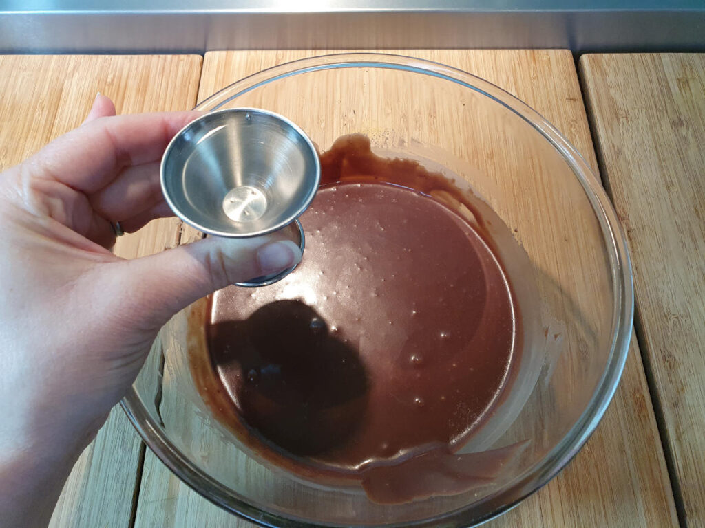 adding small shot of vodka to chocolate mix in glass bowl.