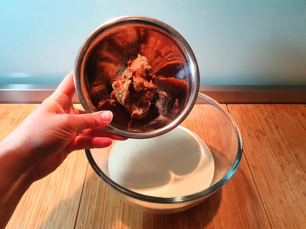 adding biscoff spread to cream in a glass bowl, on a chopping board.