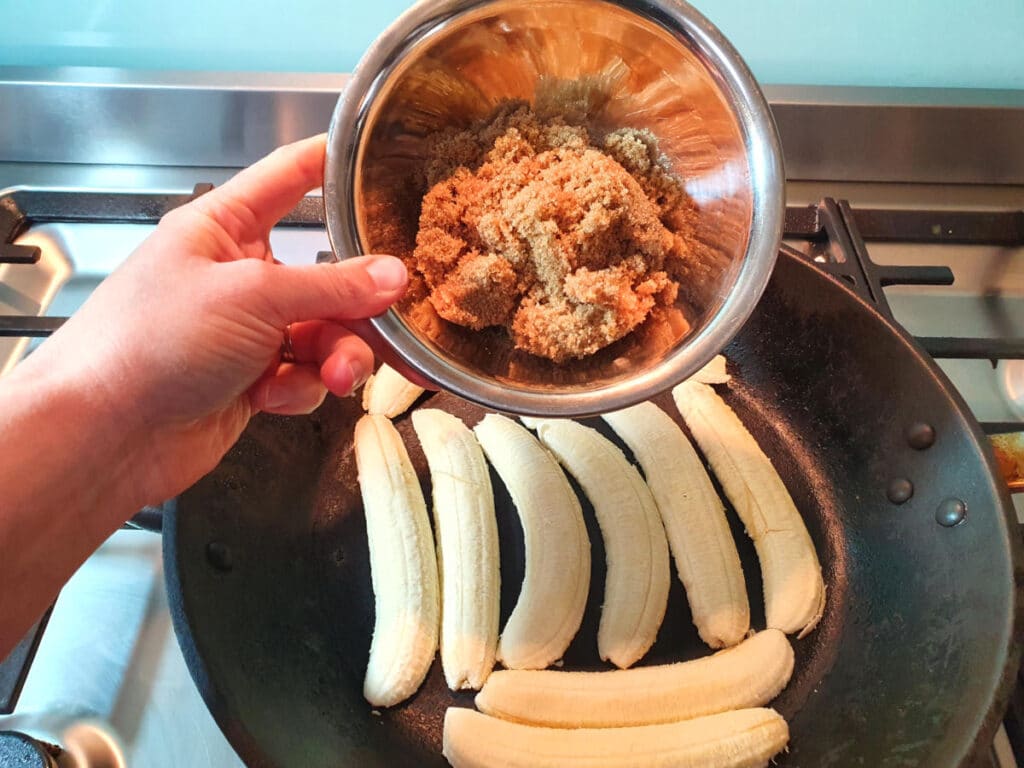 adding brown sugar to slices bananas cooking in a fry pan.