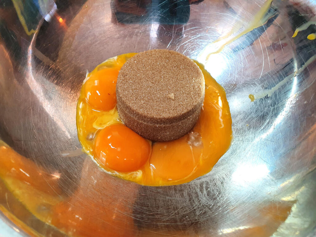 Top down view of tightly packed brown sugar and four egg yokes in a metal bowl.
