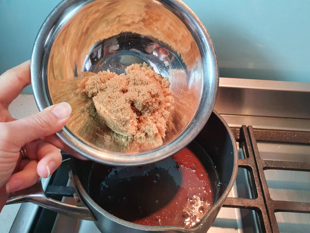 adding brown sugar to pot on stove with chocolate fudge sauce ingredients.