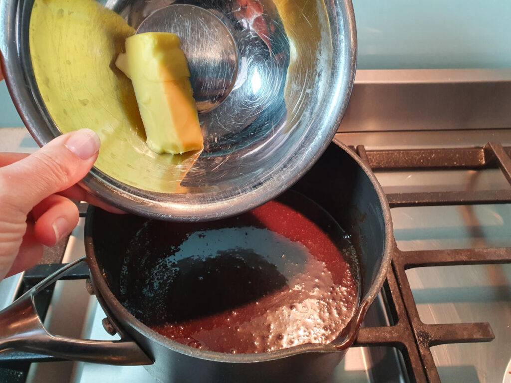 adding butter to pot on stove with chocolate fudge sauce ingredients.