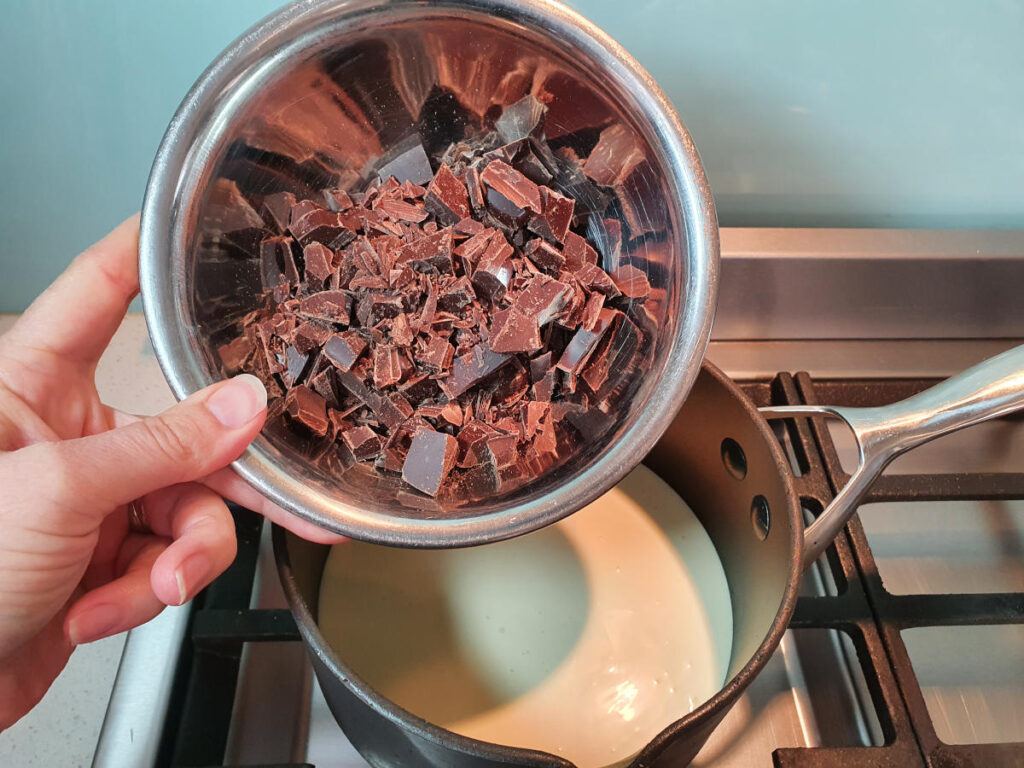 adding chocolate to pot on stove with chocolate fudge sauce ingredients.