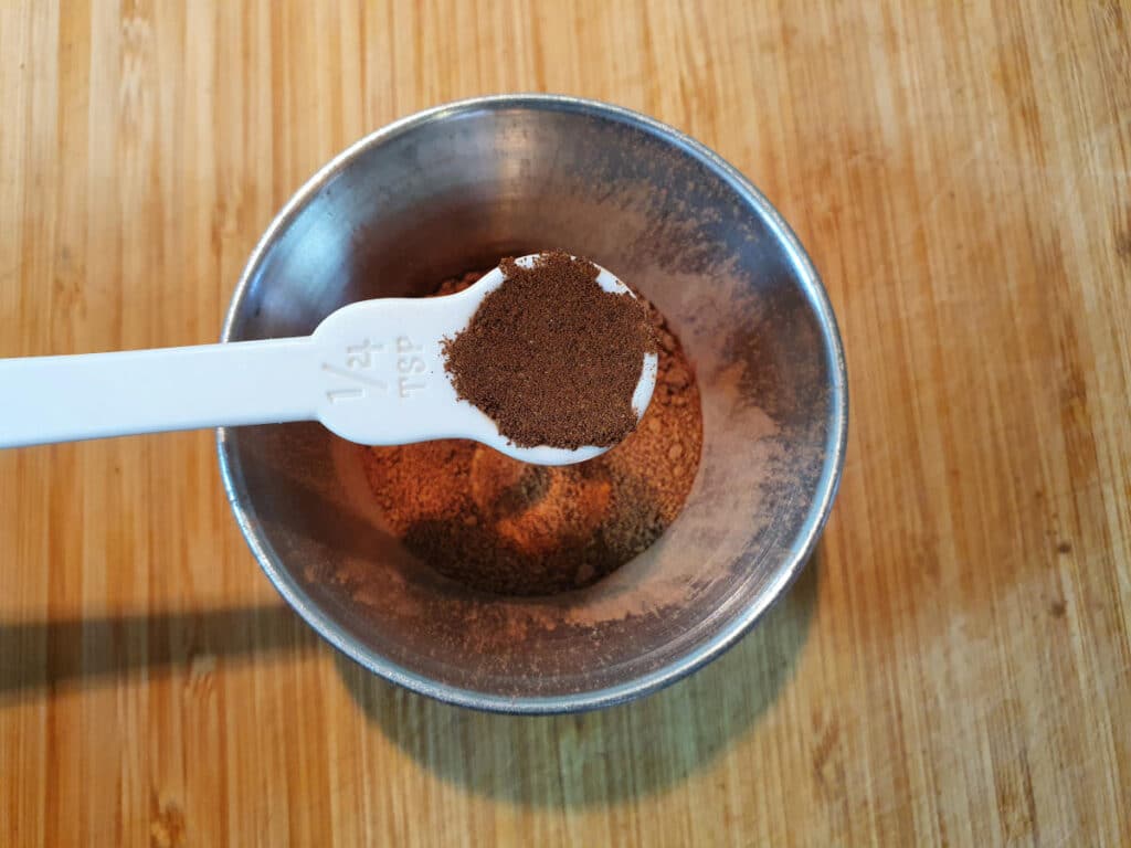 adding quarter of a teaspoon of ground cloves to a small mental bowl, on a chopping board.