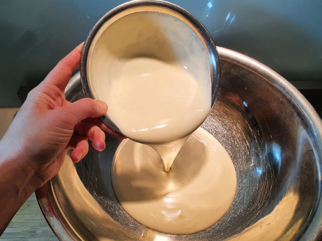 adding cream to a large metal bowl.