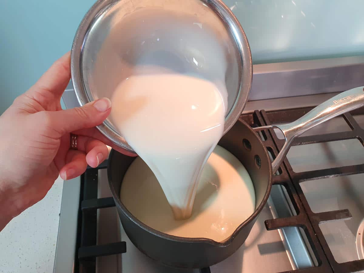 Pumpkin spice ice cream 13 Pouring cream from a metal bowl into a small black pot on a gas stove.