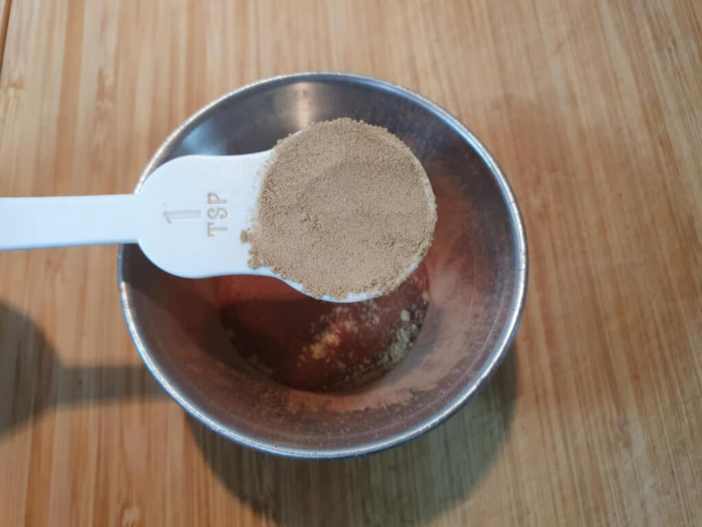 adding one teaspoon of ginger to a small mental bowl, on a chopping board.