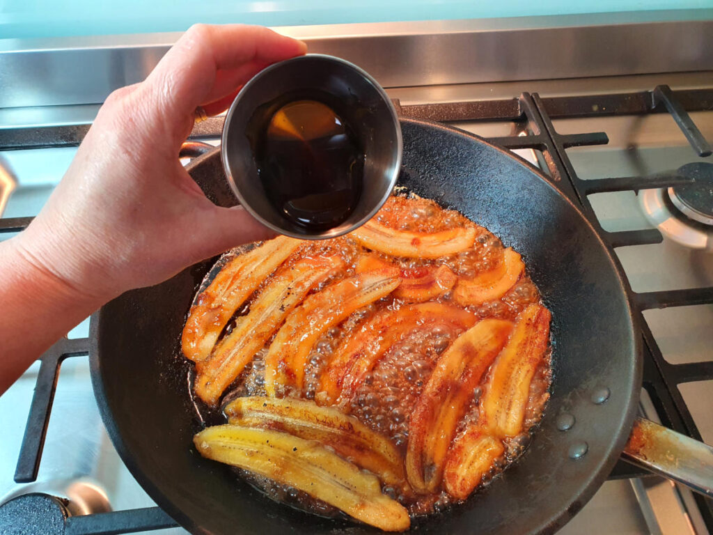 adding golden syrup to bananas, butter and brown sugar cooking in a fry pan.
