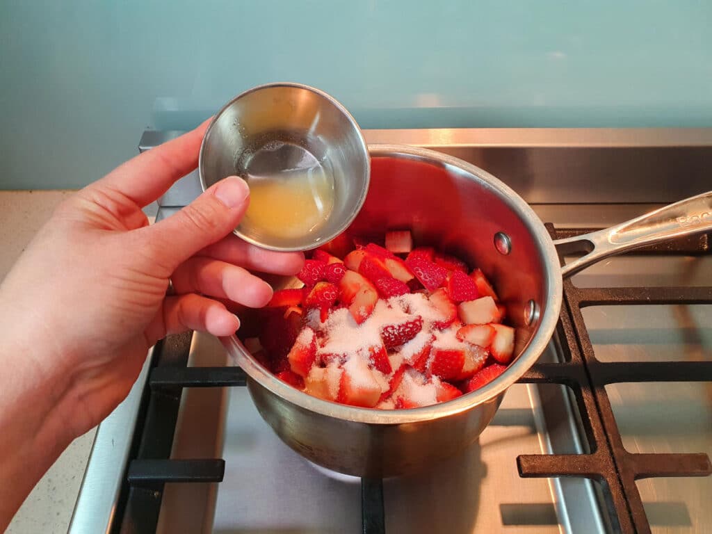 adding lemon juice to pot on stove with strawberries and sugar.
