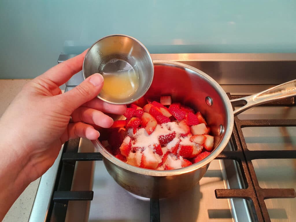 Strawberry compote (strawberry sauce) 7 adding lemon juice to pot on stove with strawberries and sugar.