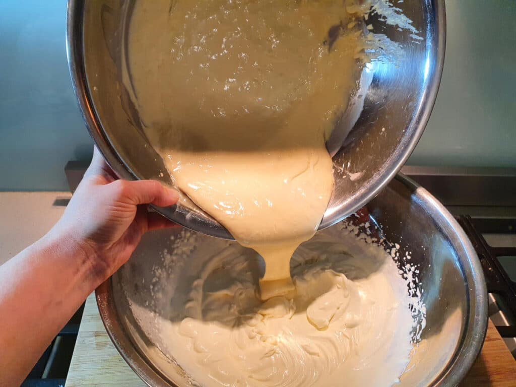 adding mascarpone mix to whipped cream in a metal bowl, on a chopping board.