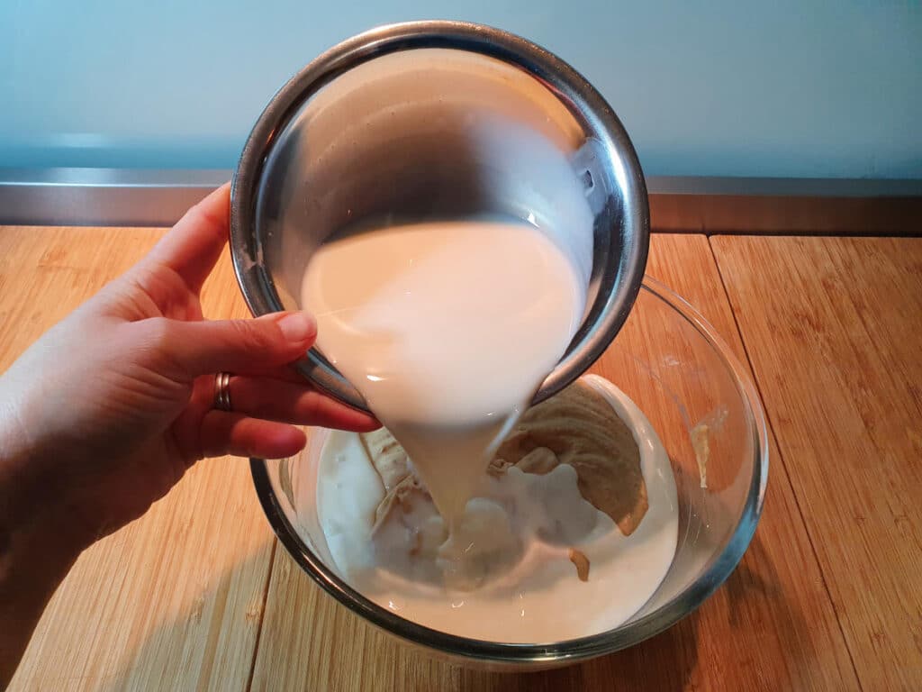 adding milk to ice cream mix in glass bowl, on a chopping board.