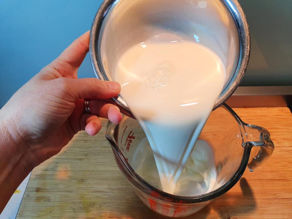 adding milk to glass jug on a chopping board.